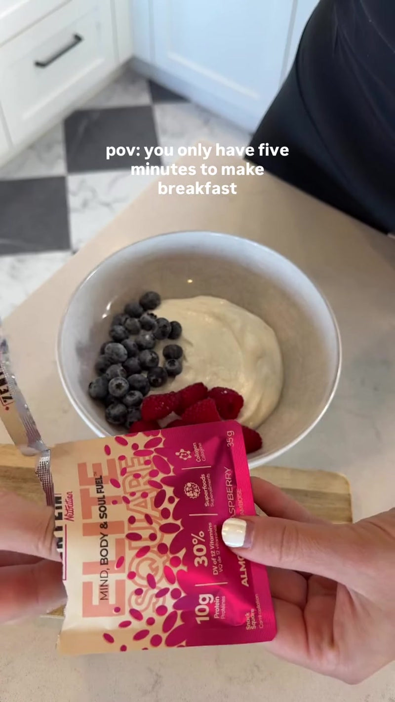 Hands chop an Almondy Raspberry Elite Square and add it to a yogurt bowl with berries.